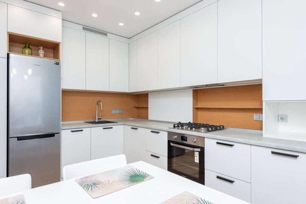 Contemporary kitchen with gas stove and oven against table with placemats and refrigerator reflecting shiny lamps in house